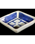 Close-up of an antique blue and white ceramic bowl with raised petal pattern, grid-textured sides, and floral center.