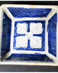 Close-up of antique blue and white ceramic bowl with raised petal center pattern and grid textured sides.