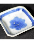 Close-up of blue and white ceramic dish with chrysanthemum bloom and geometric frame, on a dark surface.
