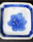 Close-up of antique blue and white ceramic dish with chrysanthemum center and blue geometric frame pattern.