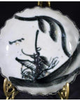 White porcelain plate with ink-style bamboo design on decorative gold stand, close-up.