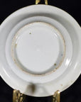 Close-up of the underside of a small antique porcelain dish with blue dashes, landscape sketch, slight rim wear, on brass stand.