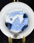Blue and white porcelain dish with landscape sketch and blue dashes, displayed on decorative metal stand.