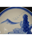 Blue and white porcelain plate with hand-painted Chinese scholar by river, antique landscape design, close-up view.