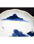 Close-up of white porcelain plate with hand-painted Chinese clouded mountain landscape and trees along rim.