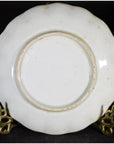 White porcelain plate with hand painted Chinese clouded mountain landscape on ornate gold stand, black background.