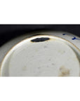 Close-up of white porcelain plate with hand-painted longevity and crab design, chipped rim, on a dark background.
