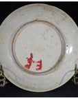 Close-up of an antique hand-painted porcelain plate with butterfly design on a metal stand, black background.
