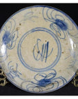 Close-up of blue and cream antique Chinese hand-painted porcelain plate with butterfly, on metal stand, dark background.