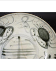 Close-up of white porcelain plate with antique painted abstract radial lines and a floral ring design.