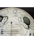 Close-up of white porcelain plate with antique painted abstract radial lines and a floral ring design.