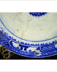 Close-up of antique ceramic plate with radial medallion, inner sunburst, loop border, visible chips and cracks.