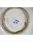White ceramic plate underside close-up with blue handwritten markings near the center, indoors.
