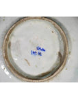 White ceramic plate underside close-up with blue handwritten markings near the center, indoors.