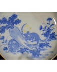 Blue and white ceramic dish with painted garden scene, featuring two mice, a radish, and floral accents.