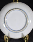 Close-up of the underside of an antique painted dish featuring mouse duo with radish, on a gold stand, dark background.