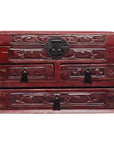 Dark red lacquered wood Chinese jewelry box with carved floral designs, multiple drawers, black metal handles, close-up.