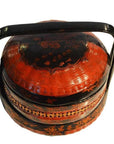 Close-up of round red and black lacquered Chinese lunch box, tiered design with handle and gold floral accents.