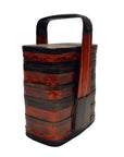 Red and black lacquered wood tiered food basket with stacked compartments and a painted handle, shown indoors.