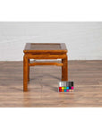 Brown elmwood Ming style waisted side table with horsehoof legs on wooden floor, color calibration card in front.
