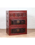 Red and black lacquered antique Chinese three-section chest with carved figures, set against a white wall.