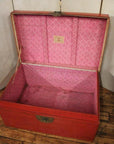 Red lacquer antique Chinese blanket chest with pink interior, open on wooden floor, light background.