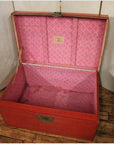 Red lacquer antique Chinese blanket chest with pink interior, open on wooden floor, light background.
