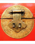 Close-up of ornate circular brass latch with floral engravings on red lacquer antique Chinese blanket chest.