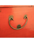 Red lacquer antique Chinese blanket chest with metal handle shaped like a smiling face, screw eyes visible.