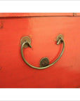 Red lacquer antique Chinese blanket chest with metal handle shaped like a smiling face, screw eyes visible.
