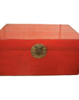 Red lacquered antique Chinese blanket chest with brass lock, on plain white background.