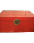 Red lacquered antique Chinese blanket chest with brass lock, on plain white background.
