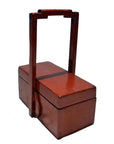 Red lacquer wood box with tall handle and two lidded compartments, antique Chinese style, close-up on plain background.