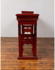 Red lacquered wood console table with carved apron on wood floor against white wall indoors.