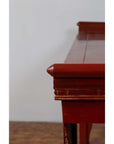 Close-up of red lacquered wood console table with carved apron detailing, plain background.