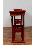 Red lacquered wood console tables with carved aprons, set indoors against a white wall on a wooden floor.