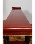 Red lacquered wood console table with carved apron, Ming style, front view on wooden flooring indoors.