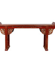 Red lacquered wood console table with carved apron against white background.