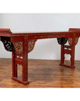 Red lacquered wood console table with carved apron, on wooden floor against a white wall.