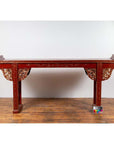 Red lacquered wood console table with carved apron, on wooden floor against a white wall indoors.