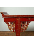 Red lacquered wood console table with carved apron and gold accents, side view.
