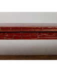 Close-up of red lacquered wood console table with carved apron, positioned indoors against a plain white wall.