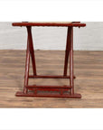 Red lacquered wood folding chair with footrest on wooden floor next to white brick wall.