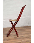 Red lacquered wood folding chair with footrest and fabric, placed indoors against a white brick wall.