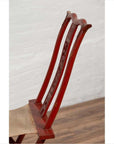 Close-up of a red lacquered wooden folding travel chair with footrest and fabric, indoors against a white wall.