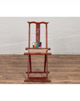 Red lacquered wood folding chair with footrest and fabric, placed on a wooden floor indoors.