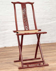 Red lacquered wood folding chair with footrest and fabric, on wooden floor by white brick wall indoors.
