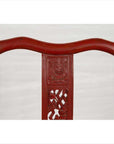 Red lacquered wood folding chair with floral carvings, footrest, fabric and metal accents, antique style.