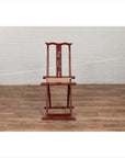 Red lacquered wood and fabric folding travel chair with footrest, indoors on wood floor against white wall.