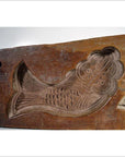 Close-up of brown antique Chinese rice mold with carved koi fish and lotus blossom designs, wooden surface background.